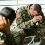 Two soldiers in military uniforms expressing emotions indoors, depicting stress and companionship.